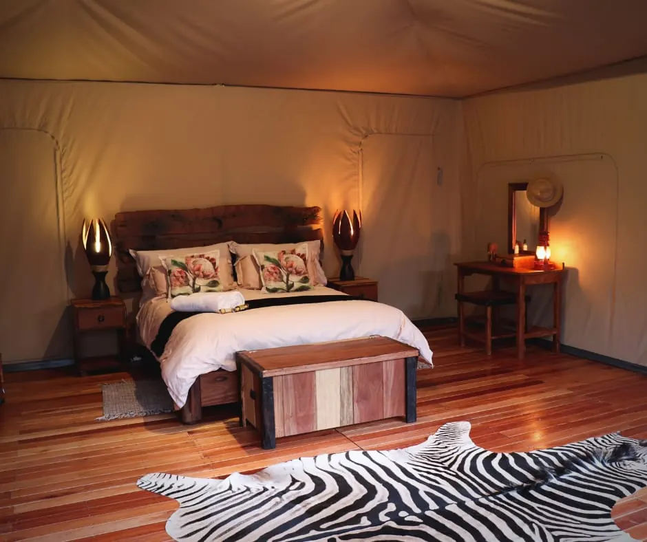 Canvas tent bedroom with timber headboard, protea cushions and zebra hide